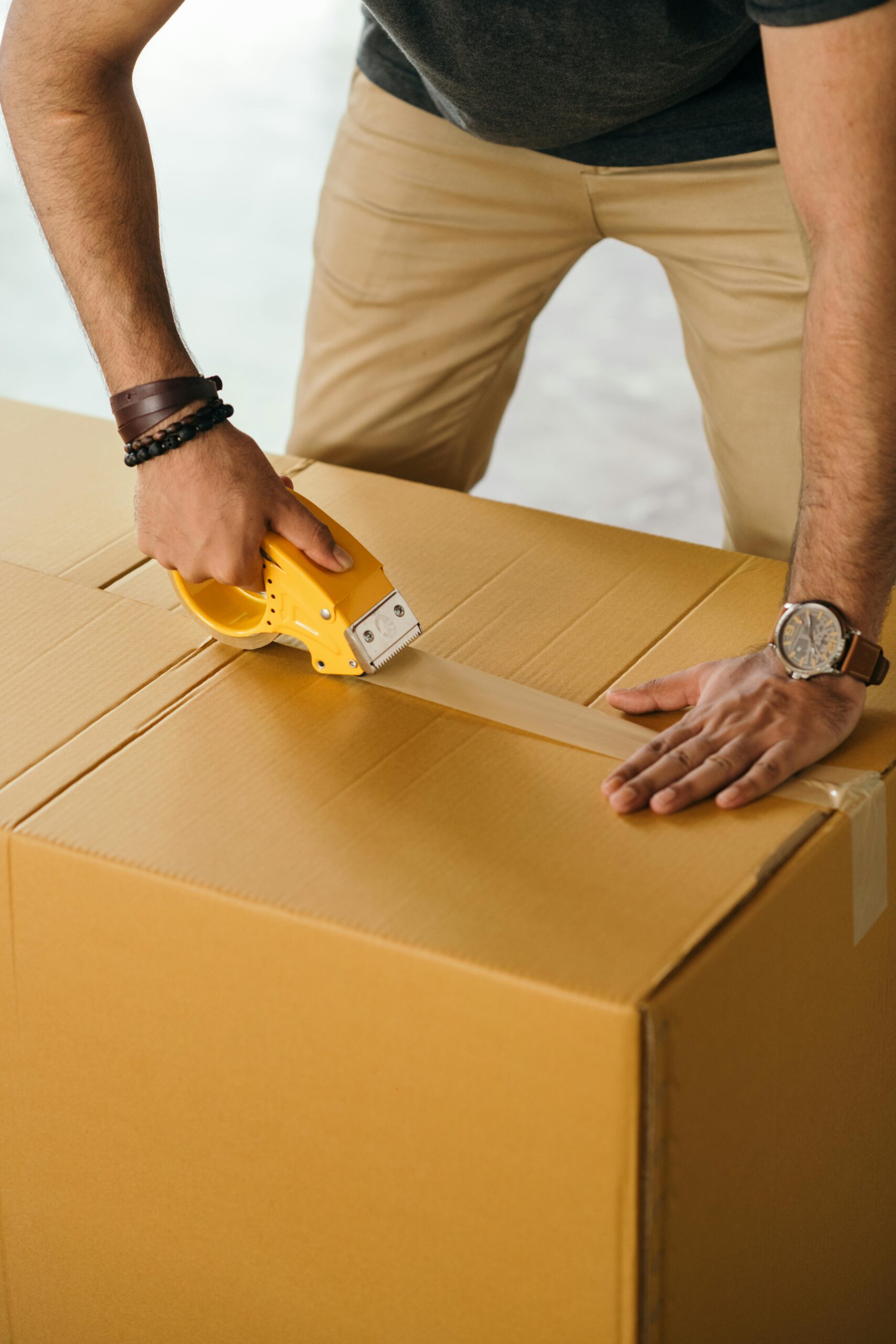 Freight Brokerage Unrecognizable man sealing box with duck tape while preparing for moving out